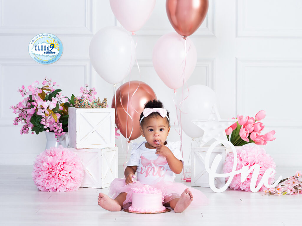 baby girl smashing her first birthday cake in a simple pink and white color themed setting at Cloud 9 Studios