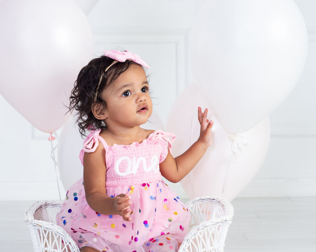Baby girl looking up with wonder as she plays with her balloons during First Birthday Session at Cloud 9 Studios in Wesley Chapel, Florida just north of Tampa