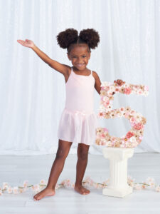 a five year old girl saying "ta da" as she proudly holds her number 5 in a ballet pose at Cloud 9 Studios in Wesley Chapel, Florida