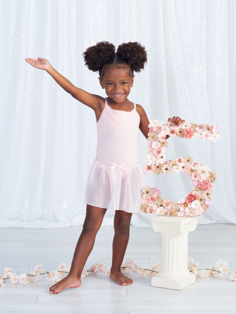 a five year old girl saying "ta da" as she proudly holds her number 5 in a ballet pose at Cloud 9 Studios in Wesley Chapel, Florida