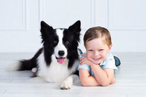Young boy lying beside his dog in a studio portrait, both smiling at the camera during a child and pet photography session.