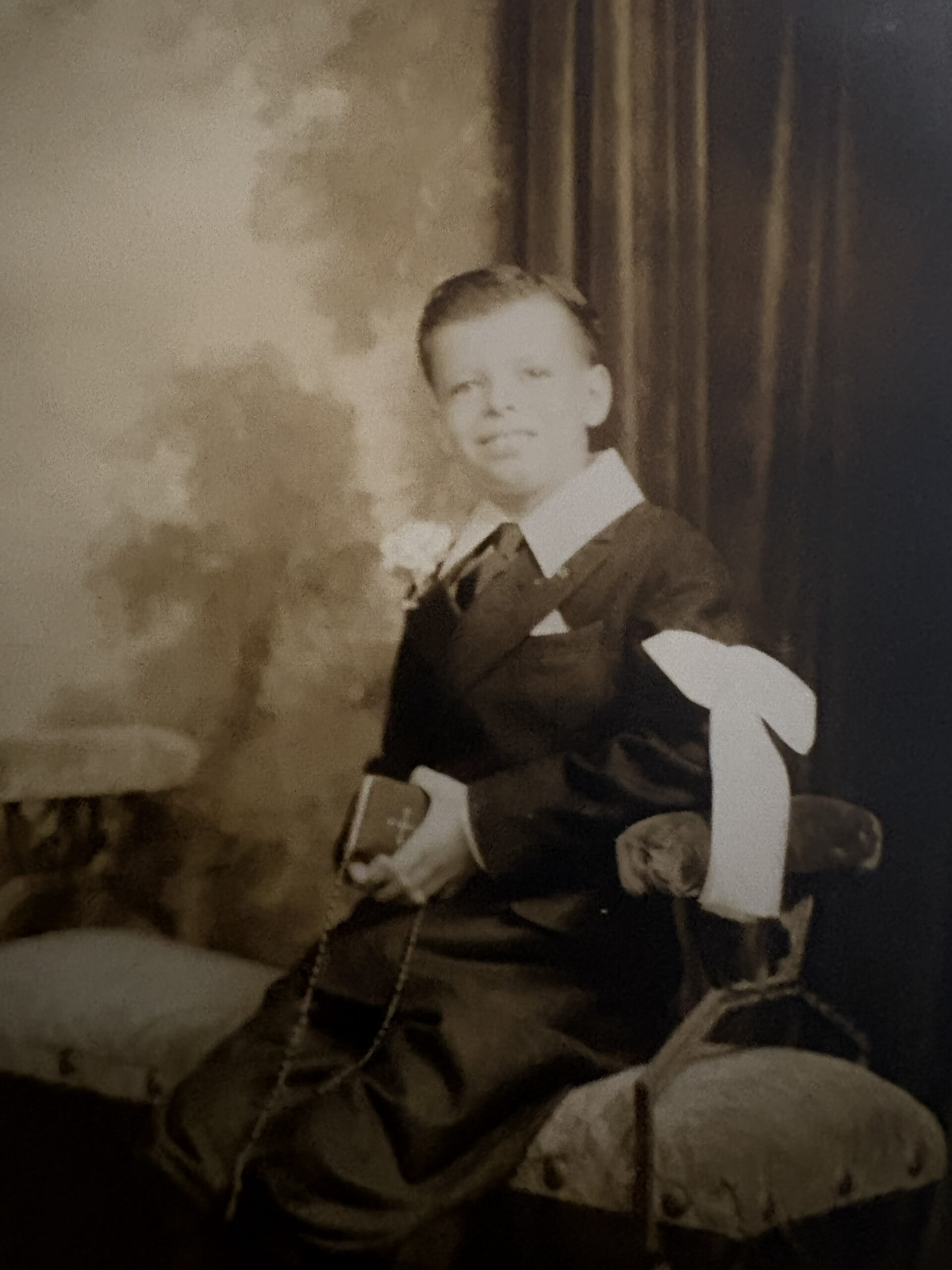 First Communion portrait of a young boy in a dark suit holding a Bible and rosary, circa 1930s, New York City