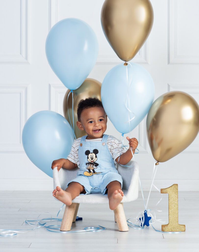 baby boy smiling in his birthday chair and playing with balloons for a first birthday session at Cloud 9 studios in Wesley Chapel, Florida 