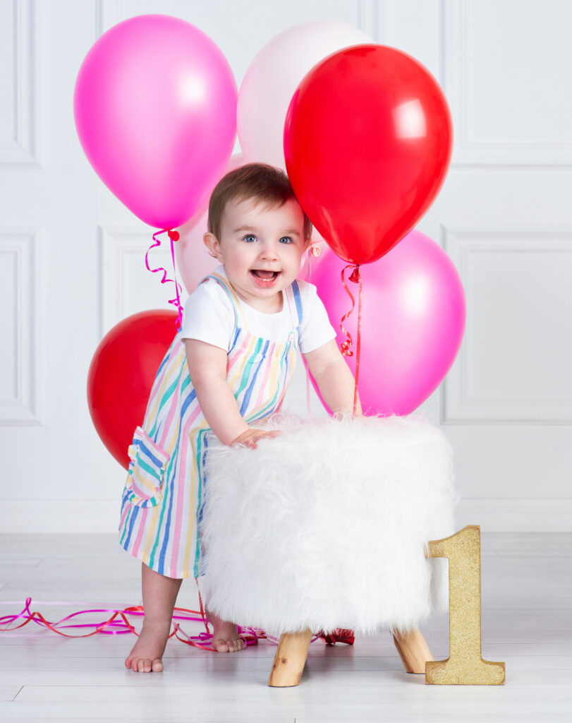 One-year-old girl playing with bright pink and red balloons during her birthday portraits