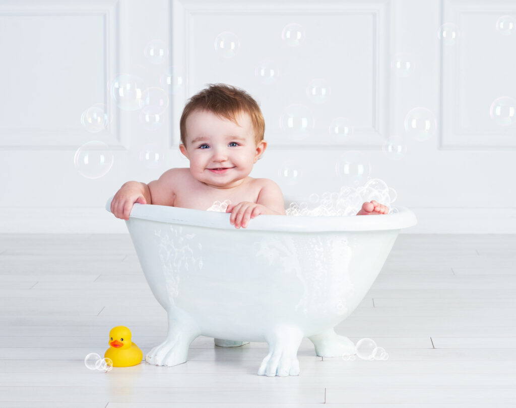 Smiling one-year-old baby playing with bubbles in the first birthday bathtub scene