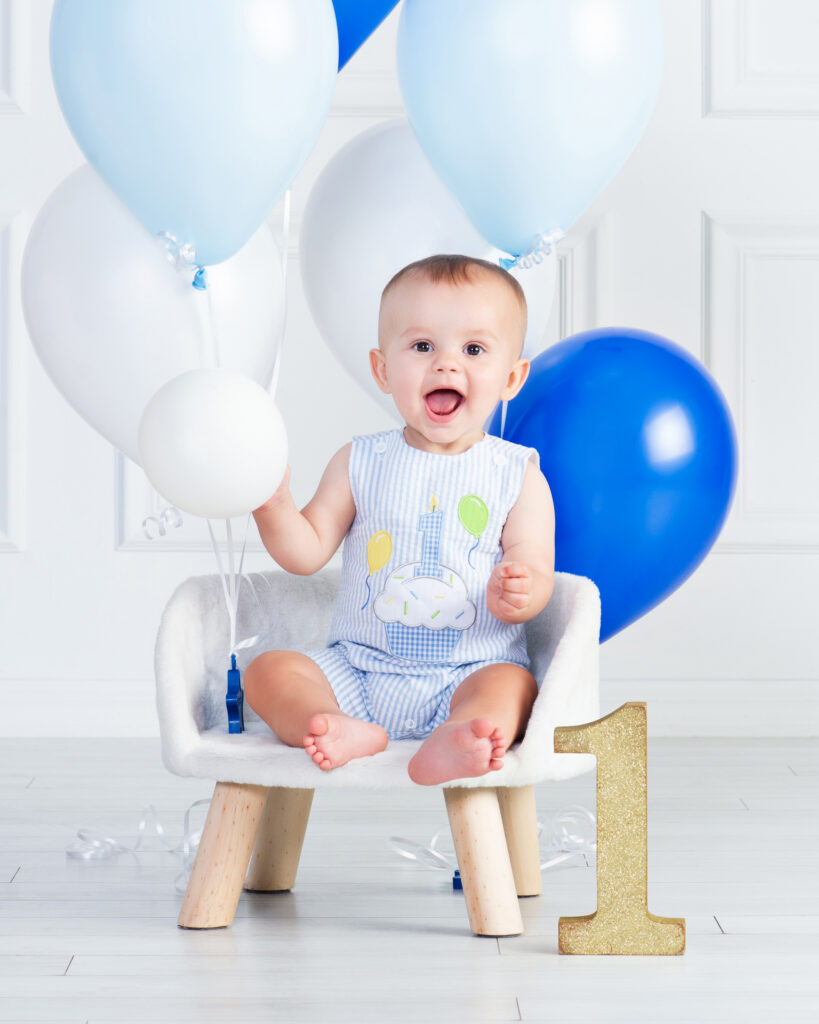 Baby boy playing with blue and white balloons during his first birthday portraits
