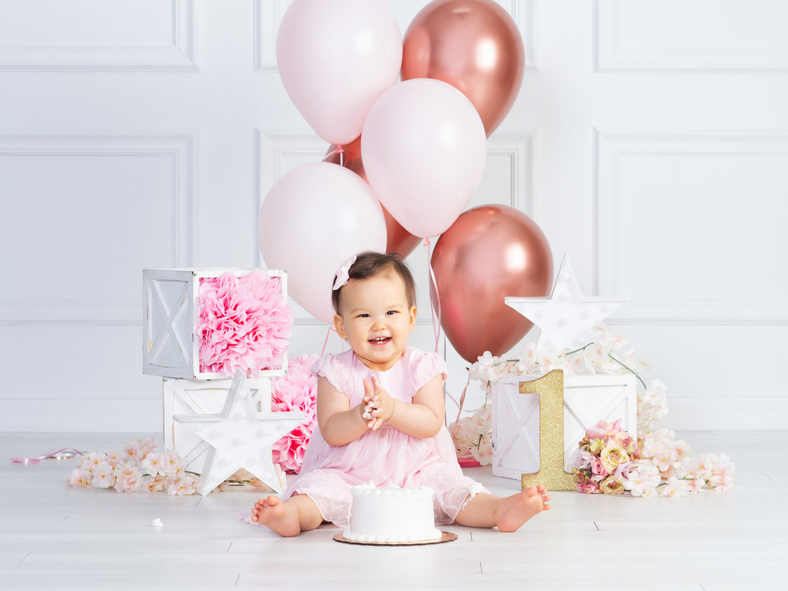 Baby girl celebrating her first birthday with pink balloons, a cake and a gold number one at Cloud 9 Studios