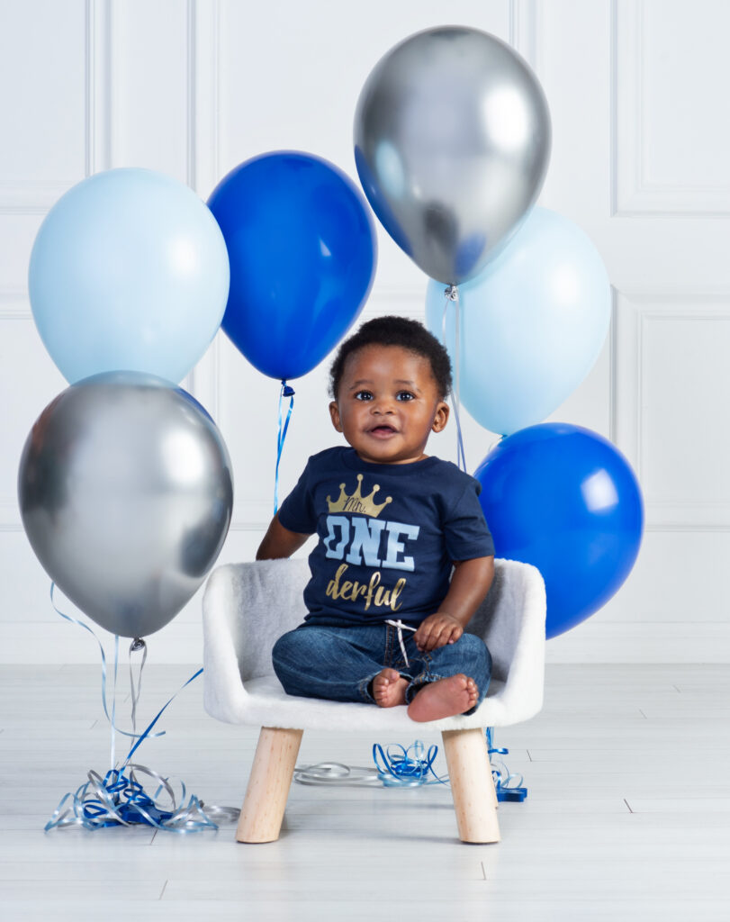 Baby boy playing with blue and white balloons during his first birthday portraits