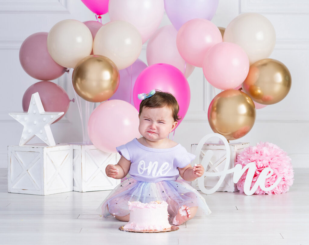 One-year-old girl crying beside her birthday cake during her first birthday portrait session