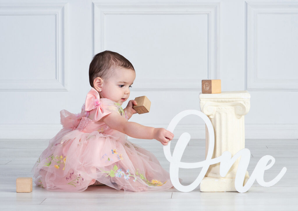One-year-old girl quietly playing with wooden blocks during her first birthday portraits