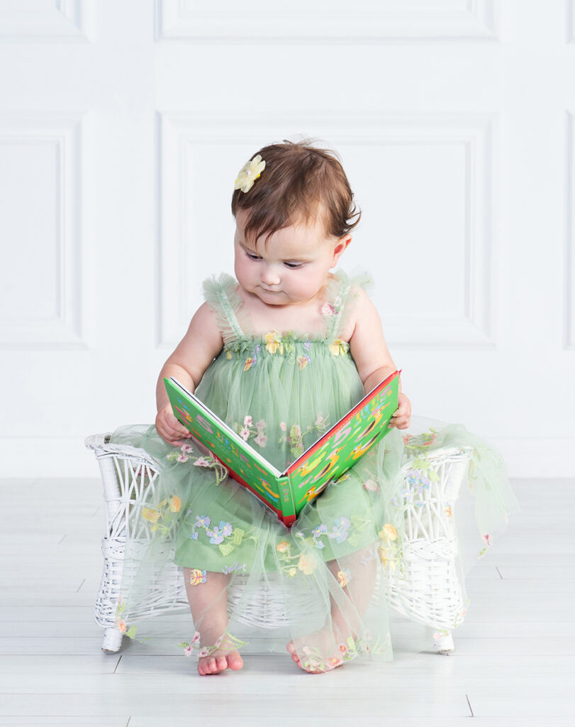 One-year-old girl quietly looking at a favorite book during her first birthday portrait session