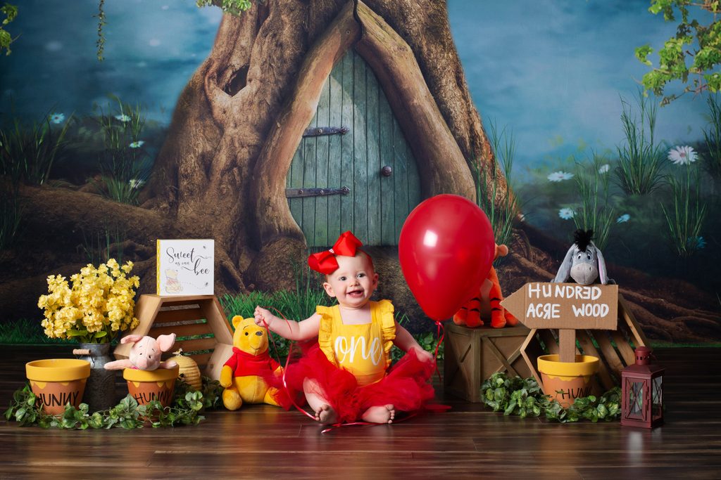 Baby girl celebrating her first birthday on a Winnie the Pooh-inspired portrait set at Cloud 9 Studios.