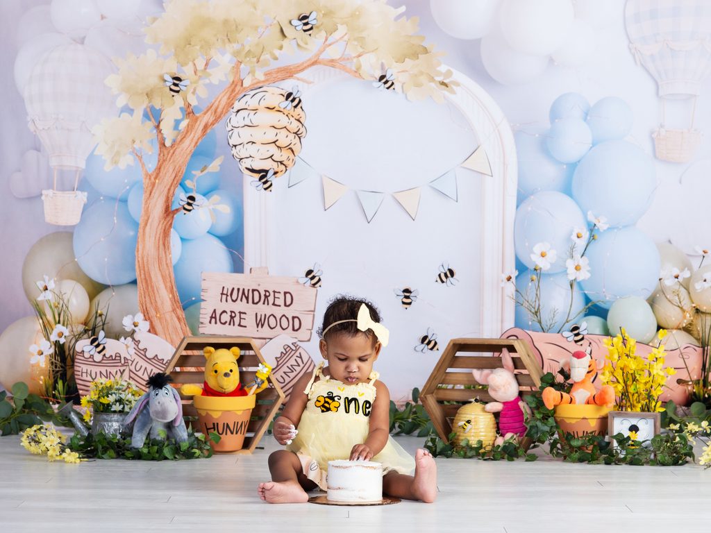 First birthday portrait of a baby girl surrounded by cheerful yellow Winnie the Pooh-inspired details.